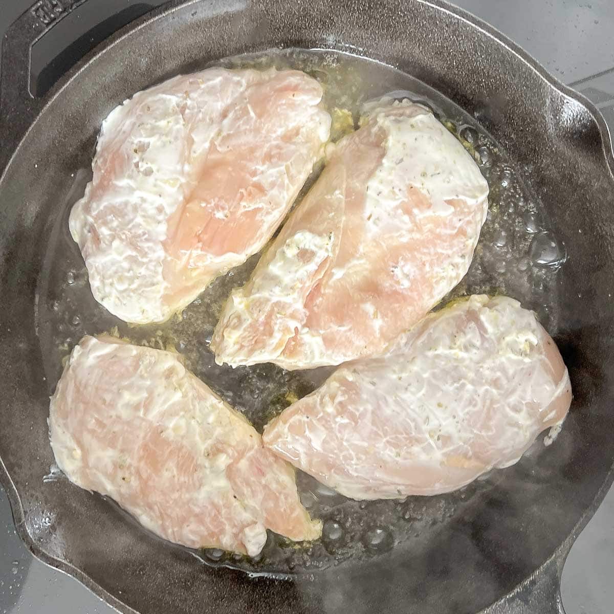 Chicken breasts in cast iron skillet, showing searing side 1