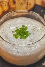 Glass bowl filled with Feta Mousse on black tray with grilled bread