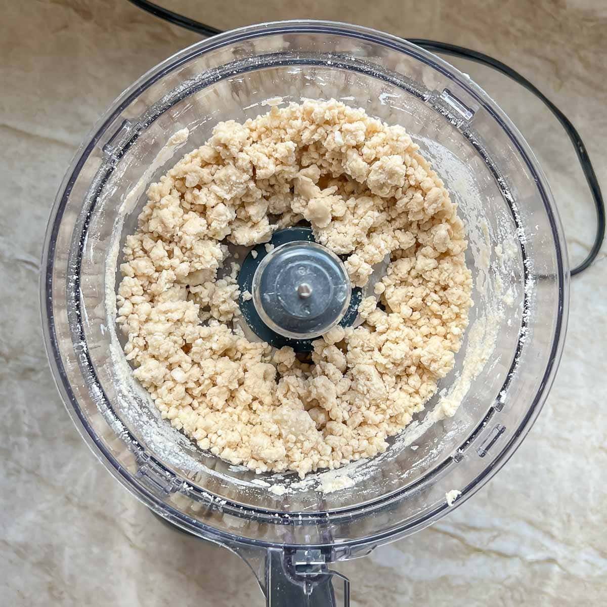 Rough dough in bowl of food processor, showing what it should look like after adding water and processing