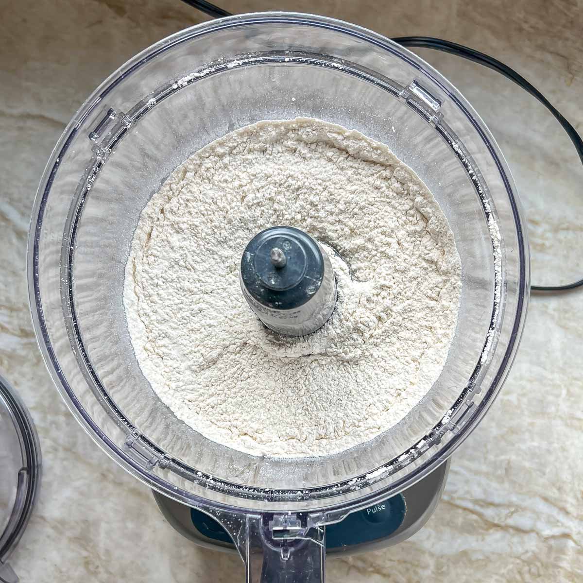 Mixed dry ingredients for flaky pie crust in the bowl of a food processor