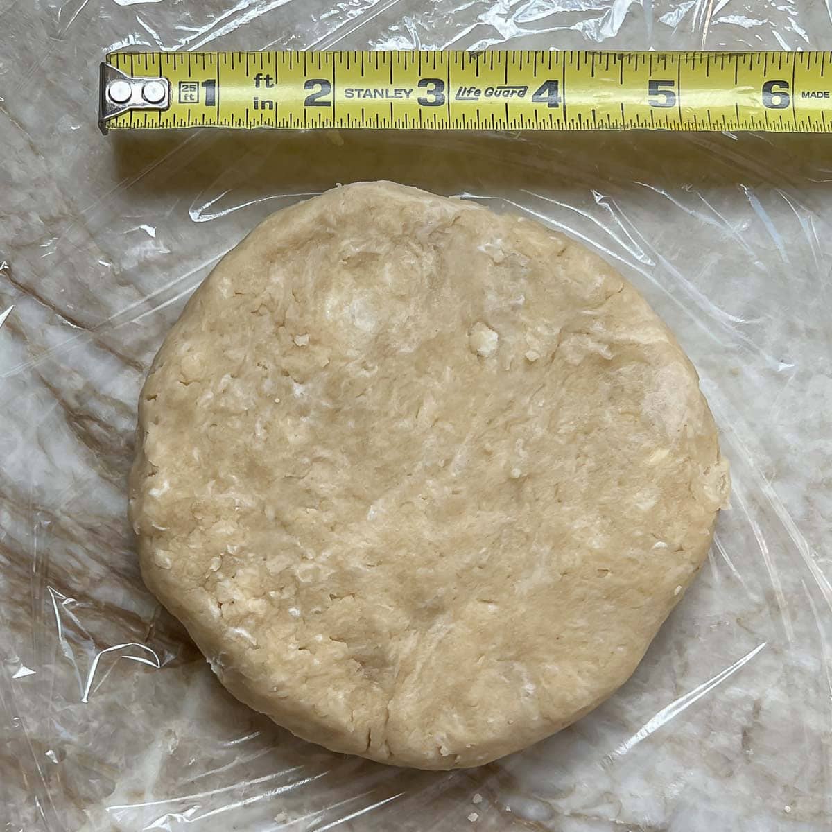 Dough rolled into a flat round disc, sitting next to a ruler showing it is 5-6 inches in diameter