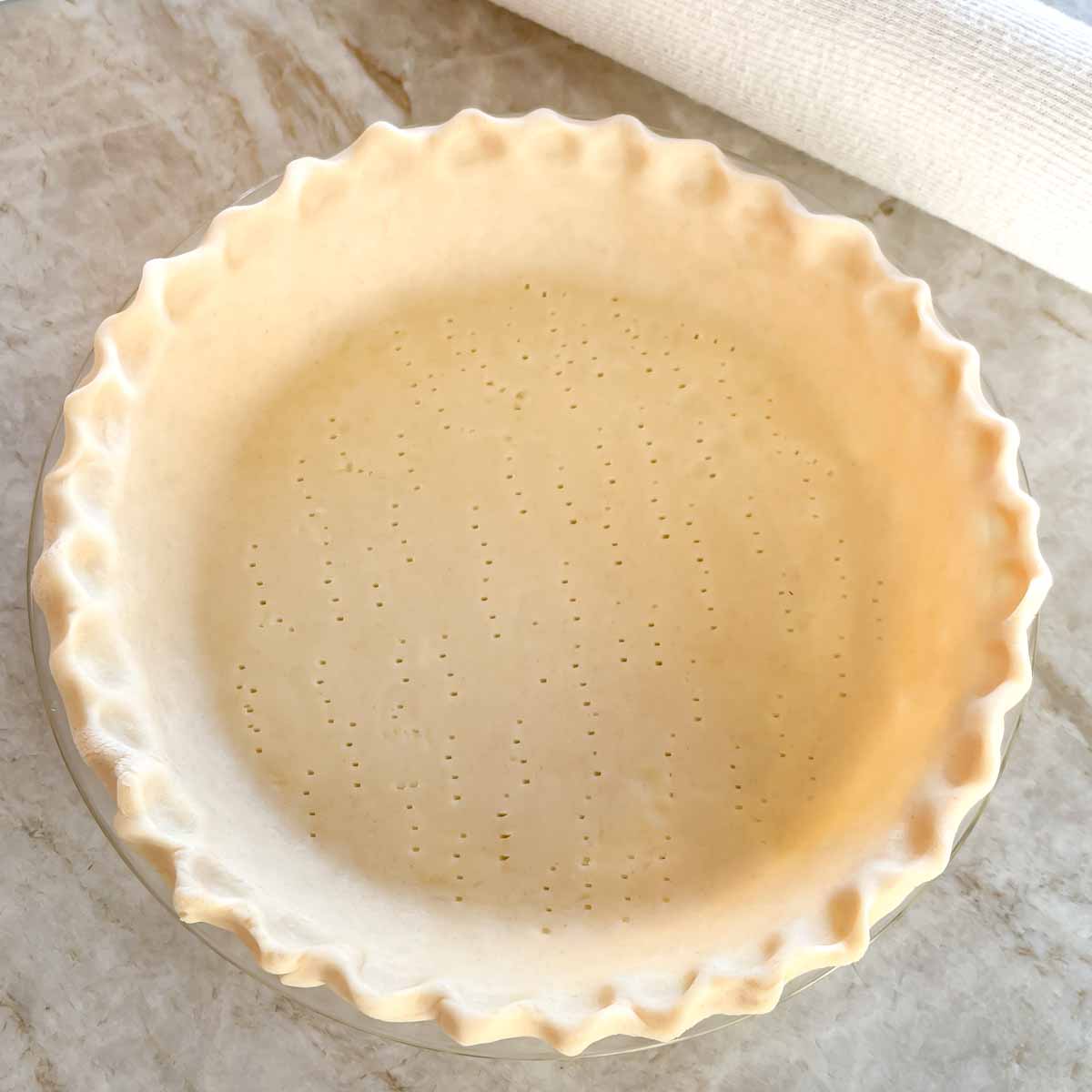 unbaked pie crust in a pie plate, with edge crimped and bottom poked with a fork