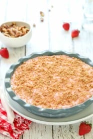 Deep dish blue pie plate showing a Frozen Strawberry Pie with walnuts in a bowl in the background