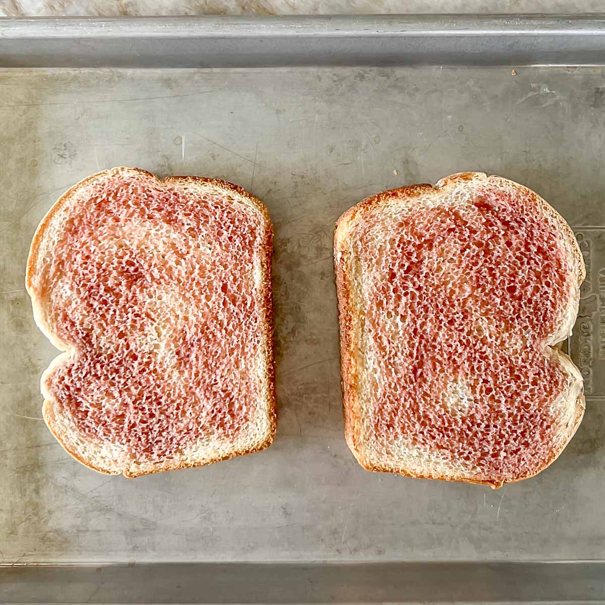 Two slices of white bread on a baking sheet, drizzled with red wine vinegar.