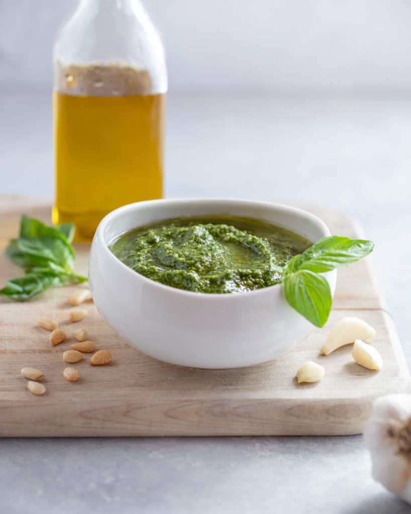 White bowl filled with Pesto Genovese, sitting on a cutting board with a bottle of olive oil in the background