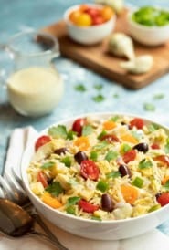 White bowl filled with Greek Orzo Salad with Lemon-Basil Tahini Dressing. Dressing is on the side