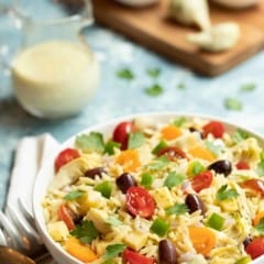 White bowl filled with Greek Orzo Salad with Lemon-Basil Tahini Dressing. Dressing is on the side