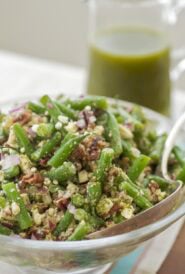 glass serving bowl holding green bean salad with mint vinaigrette in a glass pitcher in the back