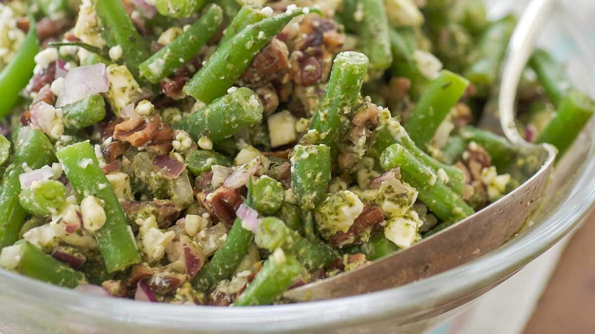 Horizontal, close view of glass serving bowl holding green bean salad with mint vinaigrette in a glass pitcher in the back