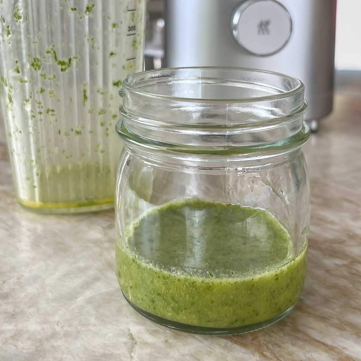 small glass jar holding mint vinaigrette, sitting in front of blender