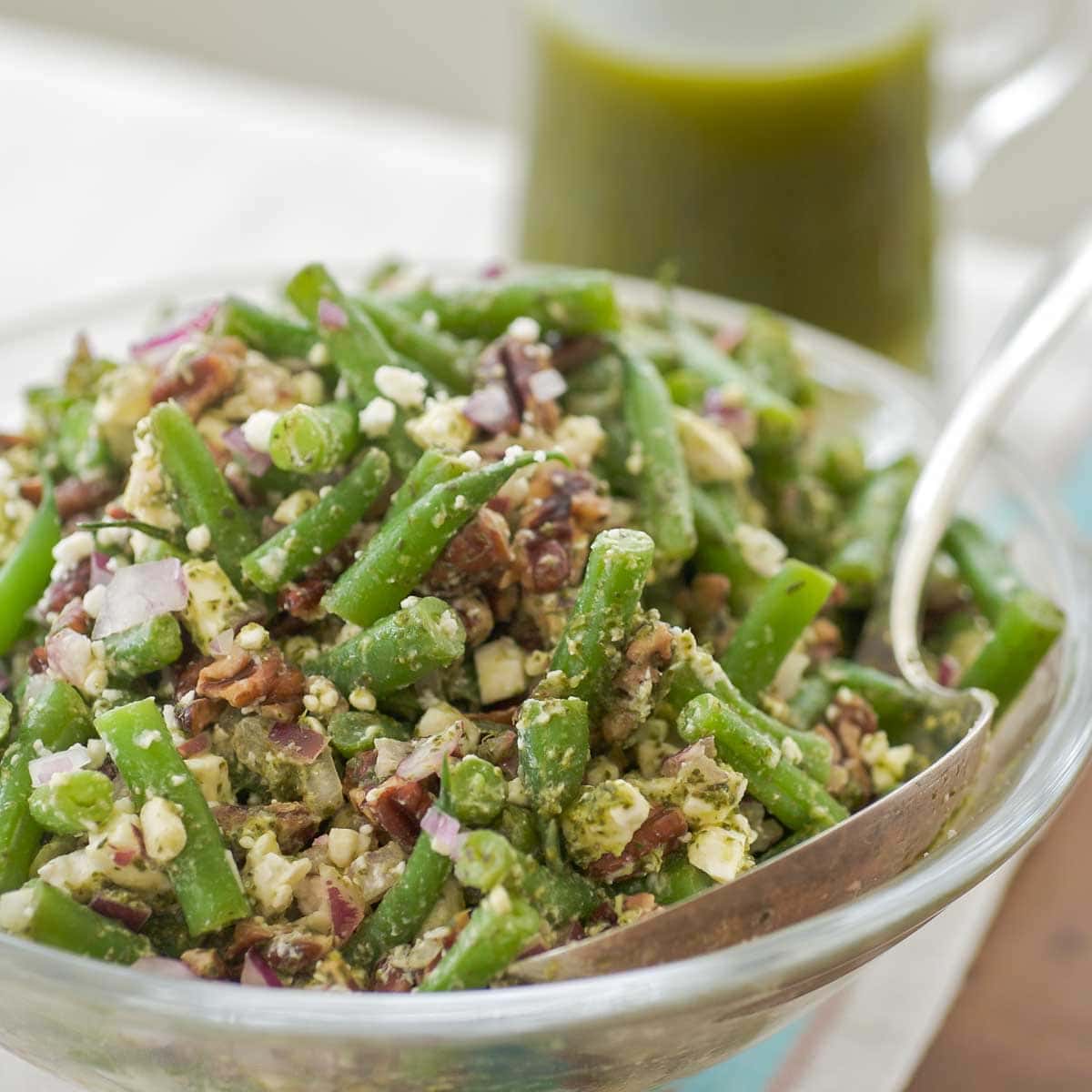 closer view of glass serving bowl holding green bean salad with mint vinaigrette in a glass pitcher in the back