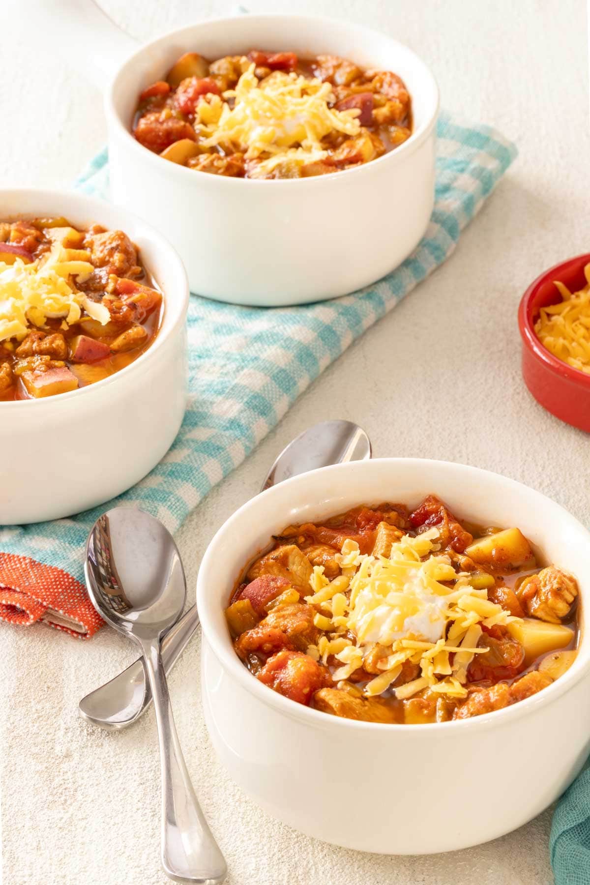 White soup bowl holding a single serving of Green Chile Chicken Soup with 2 more bowls in background
