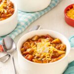 White soup bowl holding a single serving of Green Chile Chicken Soup, with 2 more bowls in background