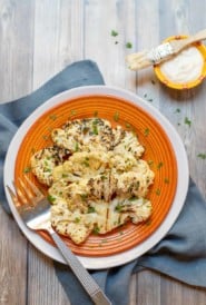 orange plate holding 2 Grilled Cauliflower Steaks with parmesan cheese on the side