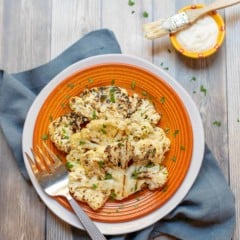 orange plate holding 2 Grilled Cauliflower Steaks with parmesan cheese on the side