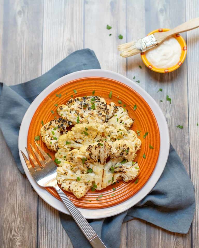 orange plate holding 2 Grilled Cauliflower Steaks with parmesan cheese on the side