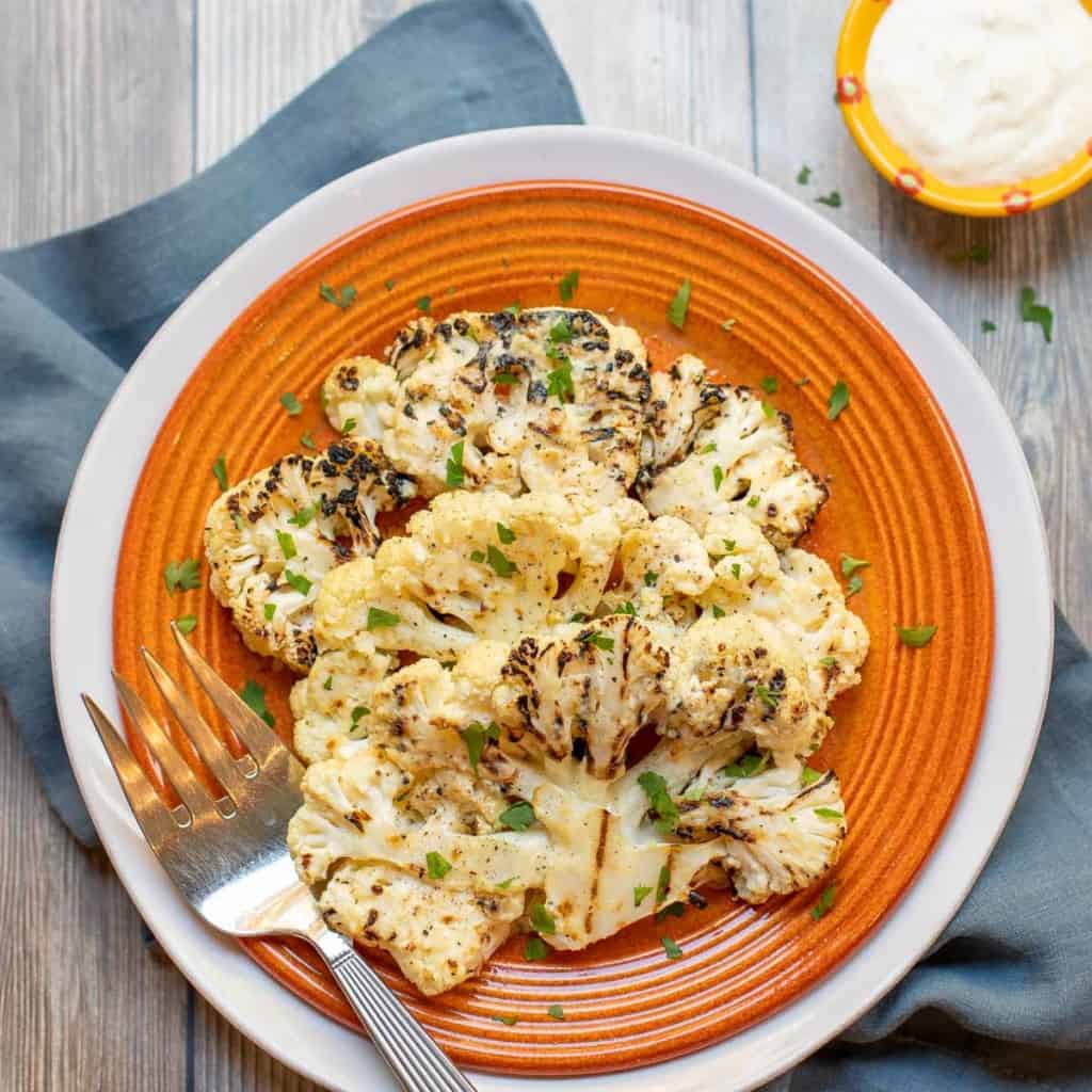 orange plate holding 2 Grilled Cauliflower Steaks with parmesan cheese on the side