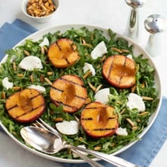Grilled peach halves and sliced Mozzarella cheese on top of baby arugula salad