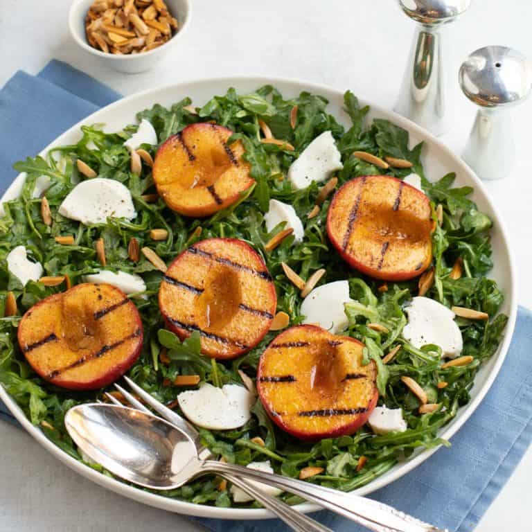 Grilled peach halves and sliced Mozzarella cheese on top of baby arugula salad