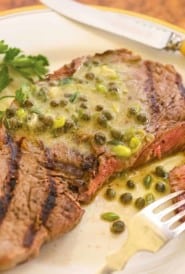 White plate holding one grilled ribeye steak, with a bite on a fork