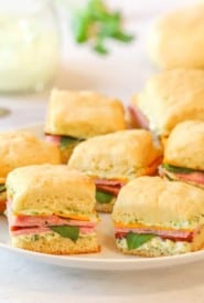 image of white plate holding several Ham and Chese Biscuits with Herb Mayo in the background