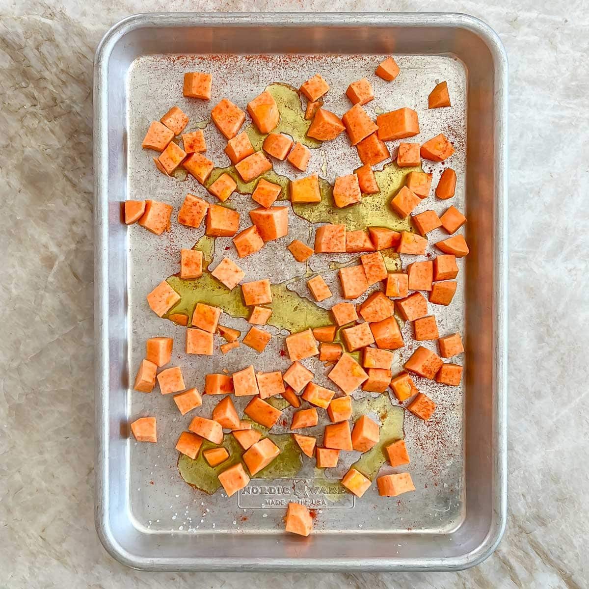 Large rimmed cookie sheet showing seasoned chopped sweet potatoes ready for roasting