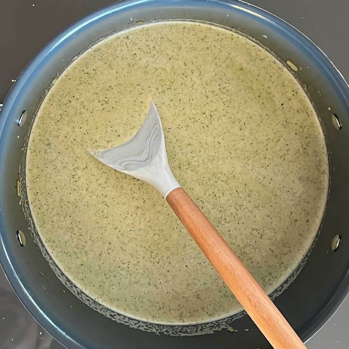 easy broccoli soup puréed with milk and soy sauce added, sitting on stovetop in a large pot with a spoon