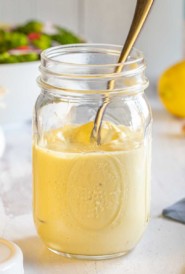 glass mason jar filled with Homemade Caesar Dressing, with a spoon inside of the jar