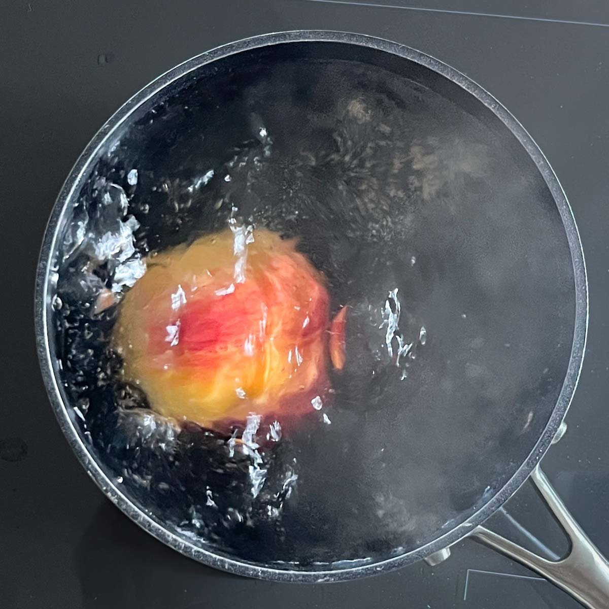 A large pot of boiling water with a single peach.