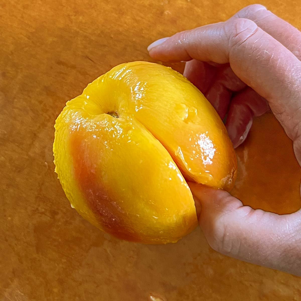 Thumb wedged in seam of peach to help split it apart.