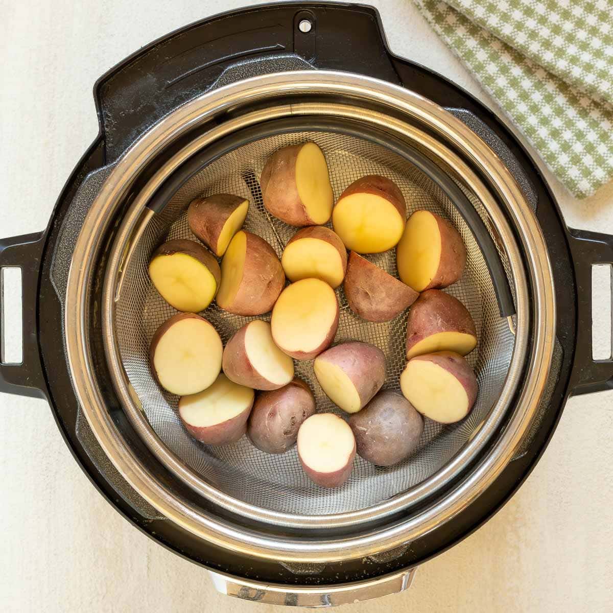 Overhead shot of uncooked, halved red potatoes inside Instant Pot steamer basket