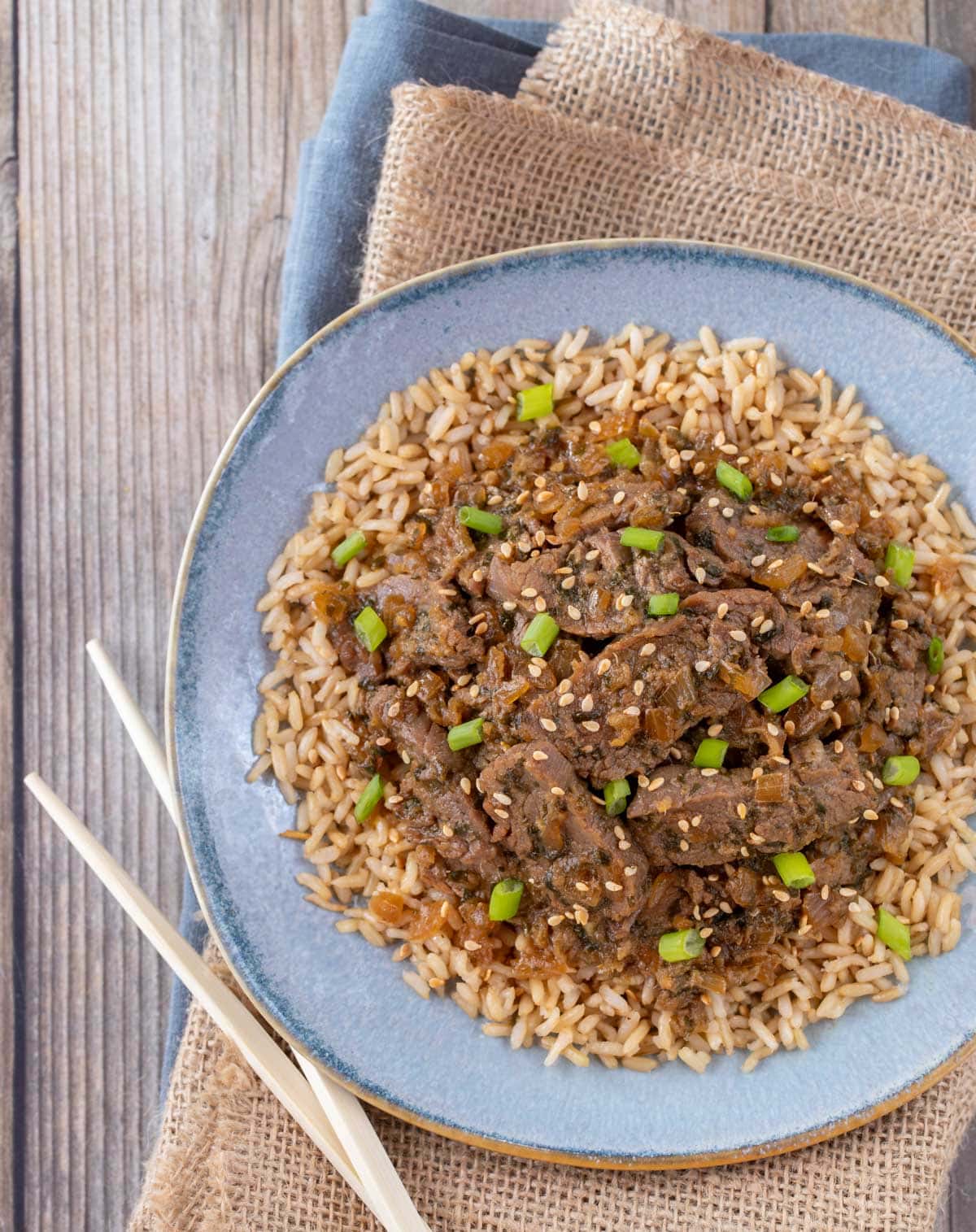 blue plate holding a large portion of Korean BBQ Beef on brown rice