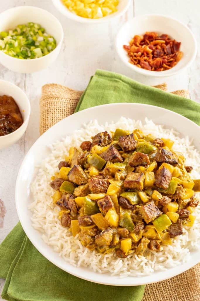 white plate holding Lamb Curry, with 4 bowls alongside showing various condiments