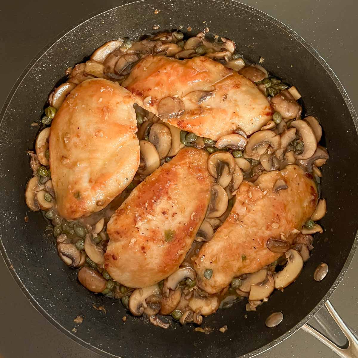 Seared chicken breasts nestled in sauce for final cooking