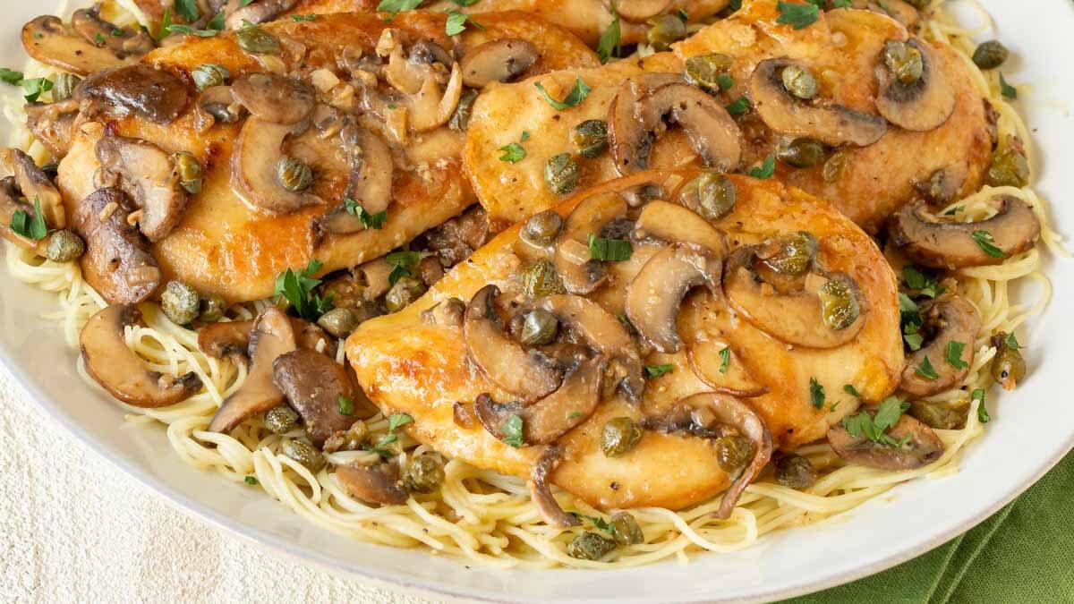 close up of Lemon Chicken Piccata with Mushrooms atop angel hair pasta
