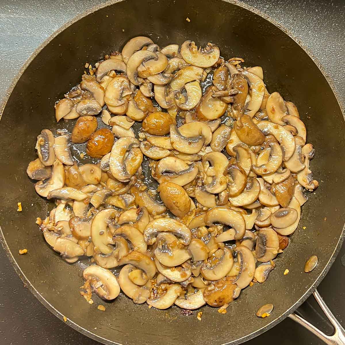 Mushrooms, garlic, and onions cooking in skillet. Shows what mushrooms look like when golden brown.