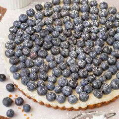 Finished Lemon Tart topped with fresh blueberries and dusted with powder sugar, with a small bowl holding more berries in back and a sifter in front