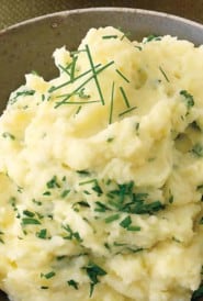 close up showing a bowl of mashed potatoes with parsley and chives