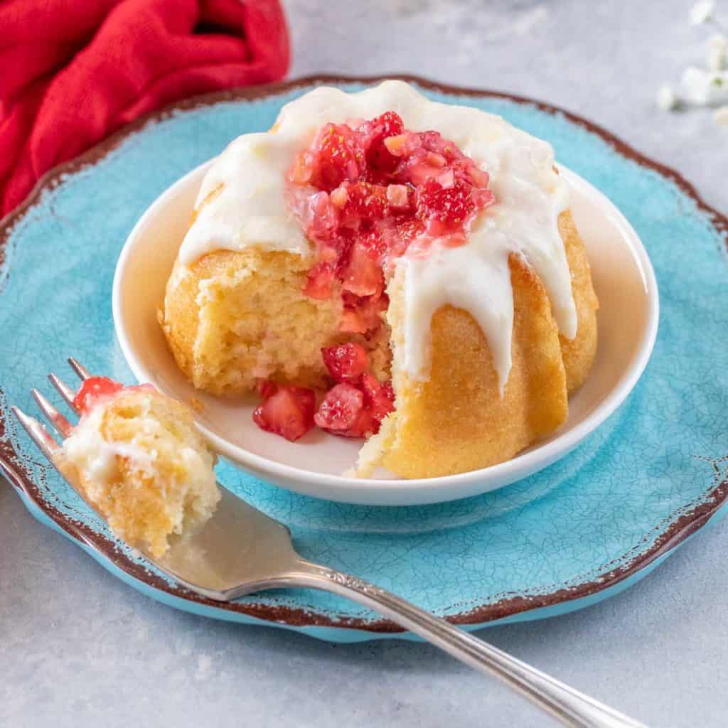 A round blue plate holding a single Mini Bundt Cake with a bite on a fork alongside.