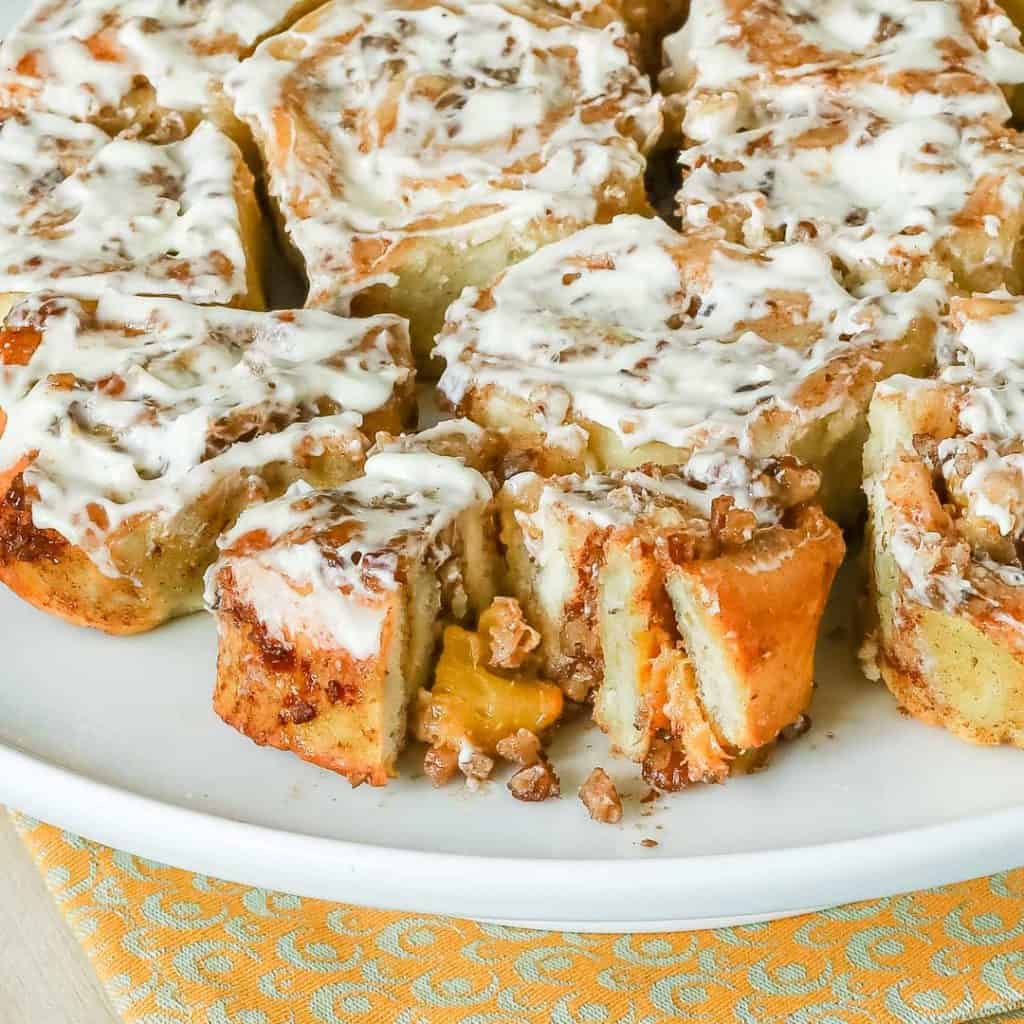 White plate holding a batch of No Yeast Cinnamon Rolls with the front roll cut open showing the peach fillling