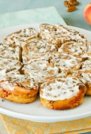 White plate holding a batch of No Yeast Cinnamon Rolls with a peach and cinnamon sticks on the side