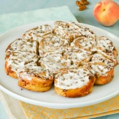 White plate holding a batch of No Yeast Cinnamon Rolls with a peach and cinnamon sticks on the side