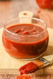 glass bowl holding Oklahoma Barbecue Sauce with a basting brush in front, with sauce on it.