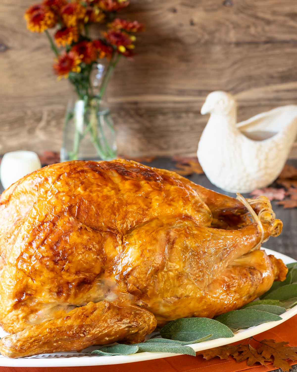 Roasted Turkey with golden brown skin on a white platter with a bird-shaped gravy boat filled with gravy behind