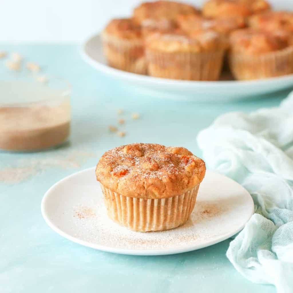 single Peach Muffin on a plate wtih a platter holding more muffins in back