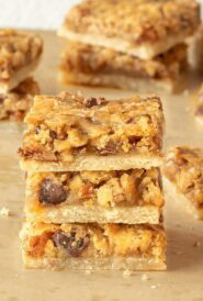 Pecan Pie Bars cut into individual bars and 3 stacked on a wooden board, showing the inside of the cookie