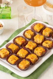 Rectangular white platter holding 15 Pimento Cheese Appetizers with Green Chiles. a cocktail and nuts are partially visible in the background.