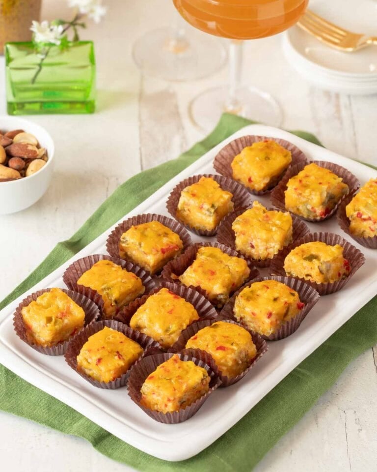 Rectangular white platter holding 15 Pimento Cheese Appetizers with Green Chiles. a cocktail and nuts are partially visible in the background.