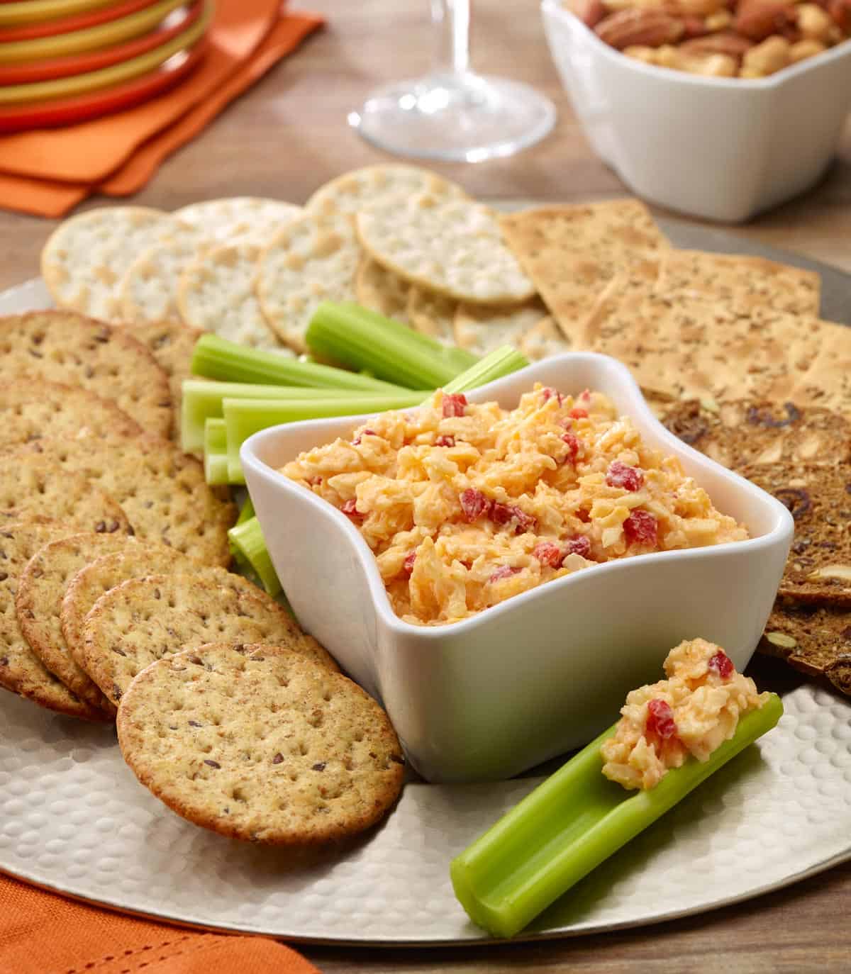 Pimiento cheese spread in a white bowl wih celery sticks and crackers