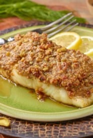 A single serving of Pistachio Crusted Fish, sitting on a light green plate that's on a cutting board.